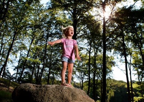 Kind steht auf großem Stein im Wald 
