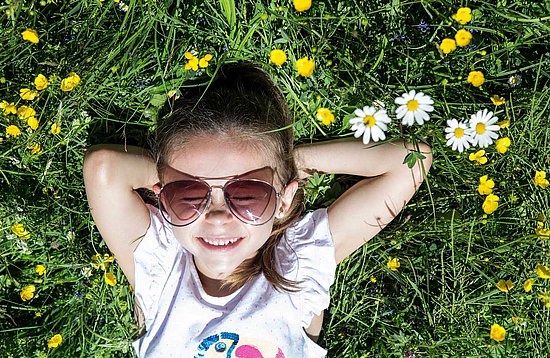 Mädchen liegt lachend mit Sonnenbrille in der Wiese 